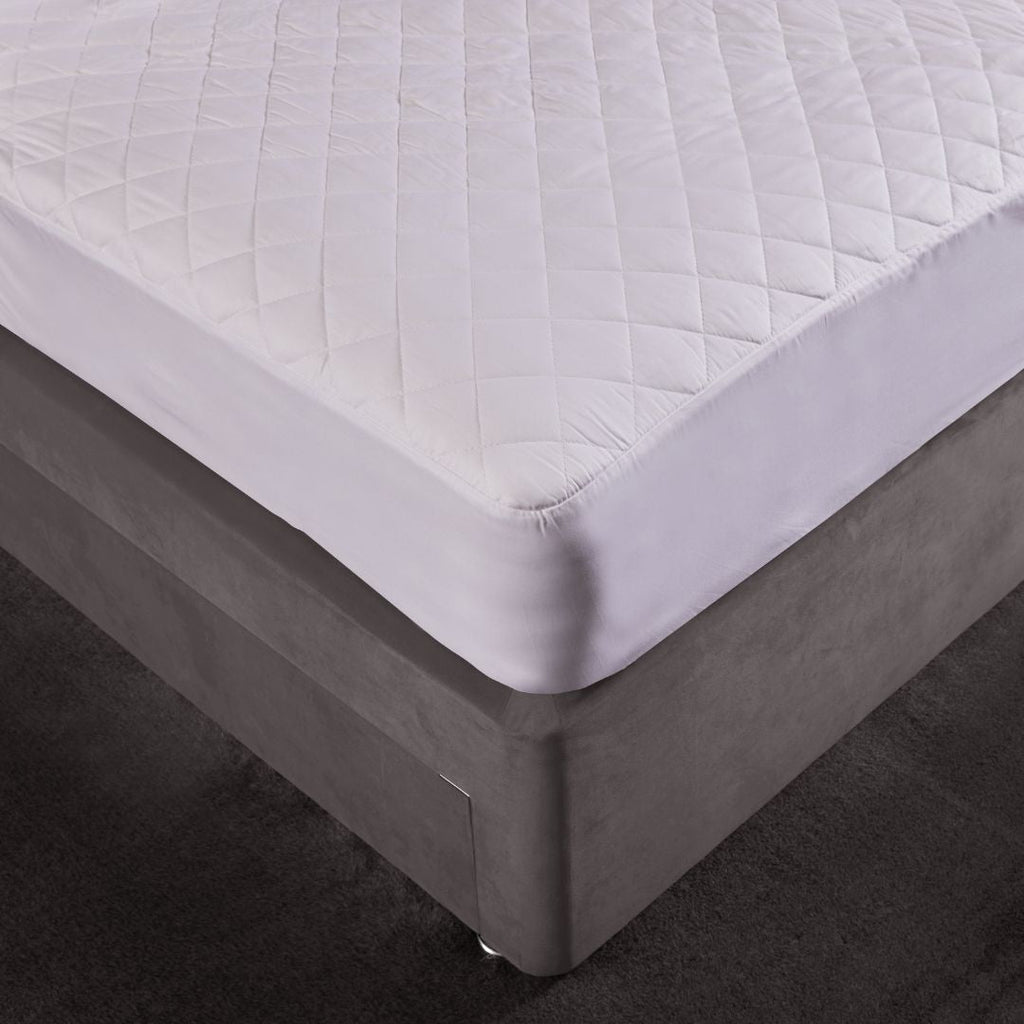 White quilted mattress protector on a bed with a dark floor.