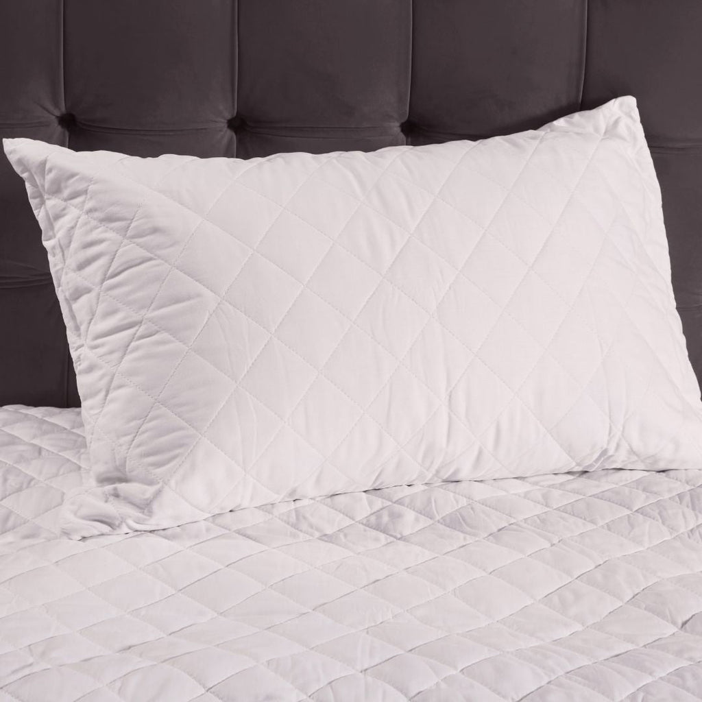 White quilted pillow on a bed with a dark headboard