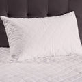 White quilted pillow on a bed with a dark headboard