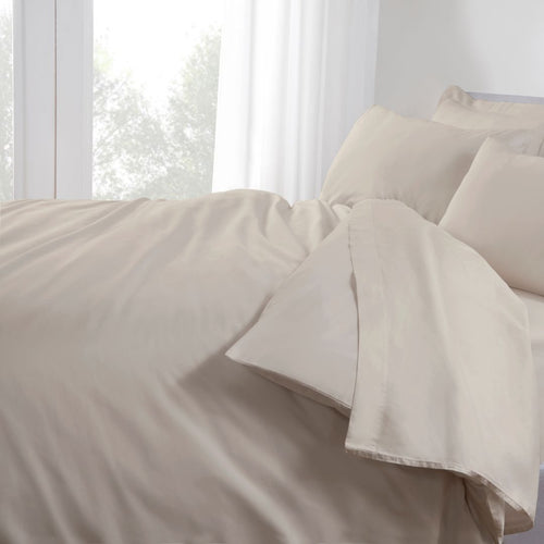 Beige bedding set on a bed with white curtains in the background