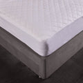 White quilted mattress protector on a bed with a dark floor.
