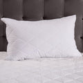 White quilted pillow on a bed with a gray headboard